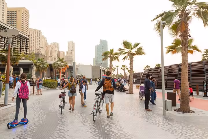Visitors exploring JBR Beach promenade on bikes and hoverboards, surrounded by palm trees and modern architecture.