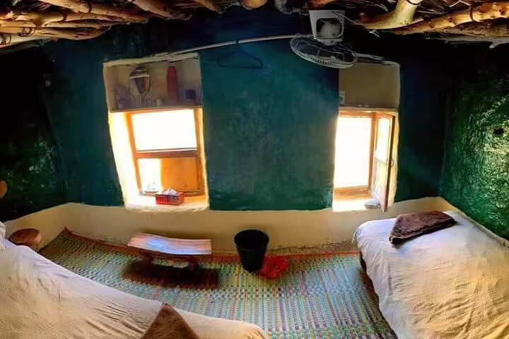 Cozy traditional room in Jebel Akhdar's Al Suwjara Village featuring rustic decor and colorful woven carpets.