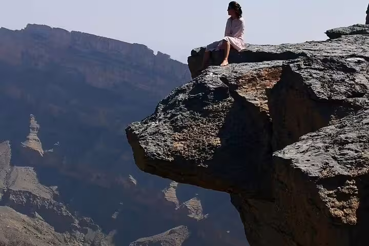 Hiker sitting on a rocky ledge with breathtaking views of Jebel Shams canyon during a private guided balcony walk.