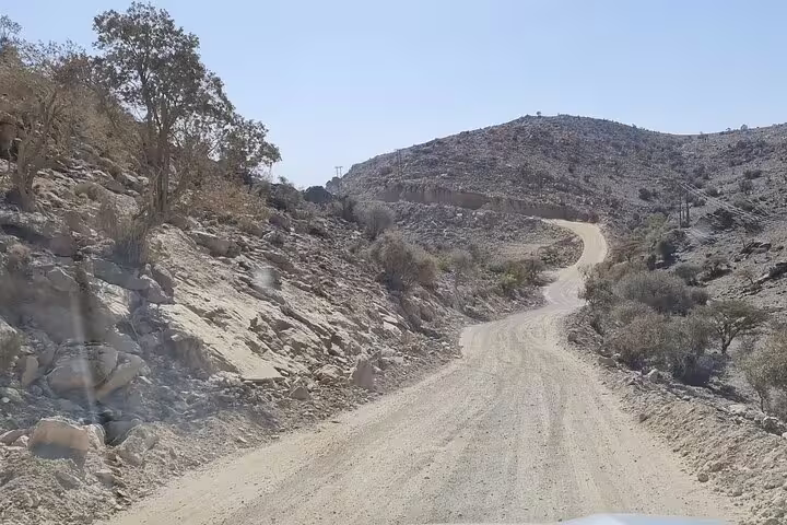 Scenic dirt road winding through rocky terrain on the way to Jebel Shams, ideal for an adventurous camping tour.