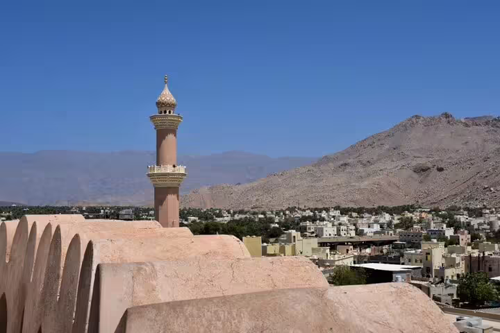 Scenic view of a mosque's minaret with a mountainous backdrop and traditional village at Jebel Shams, Oman, perfect for cultural tours.