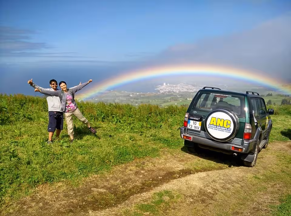 Couple on Jeep off-road tour in Sete Cidades posing by 4x4 with vivid rainbow over Azores volcanic crater landscape
