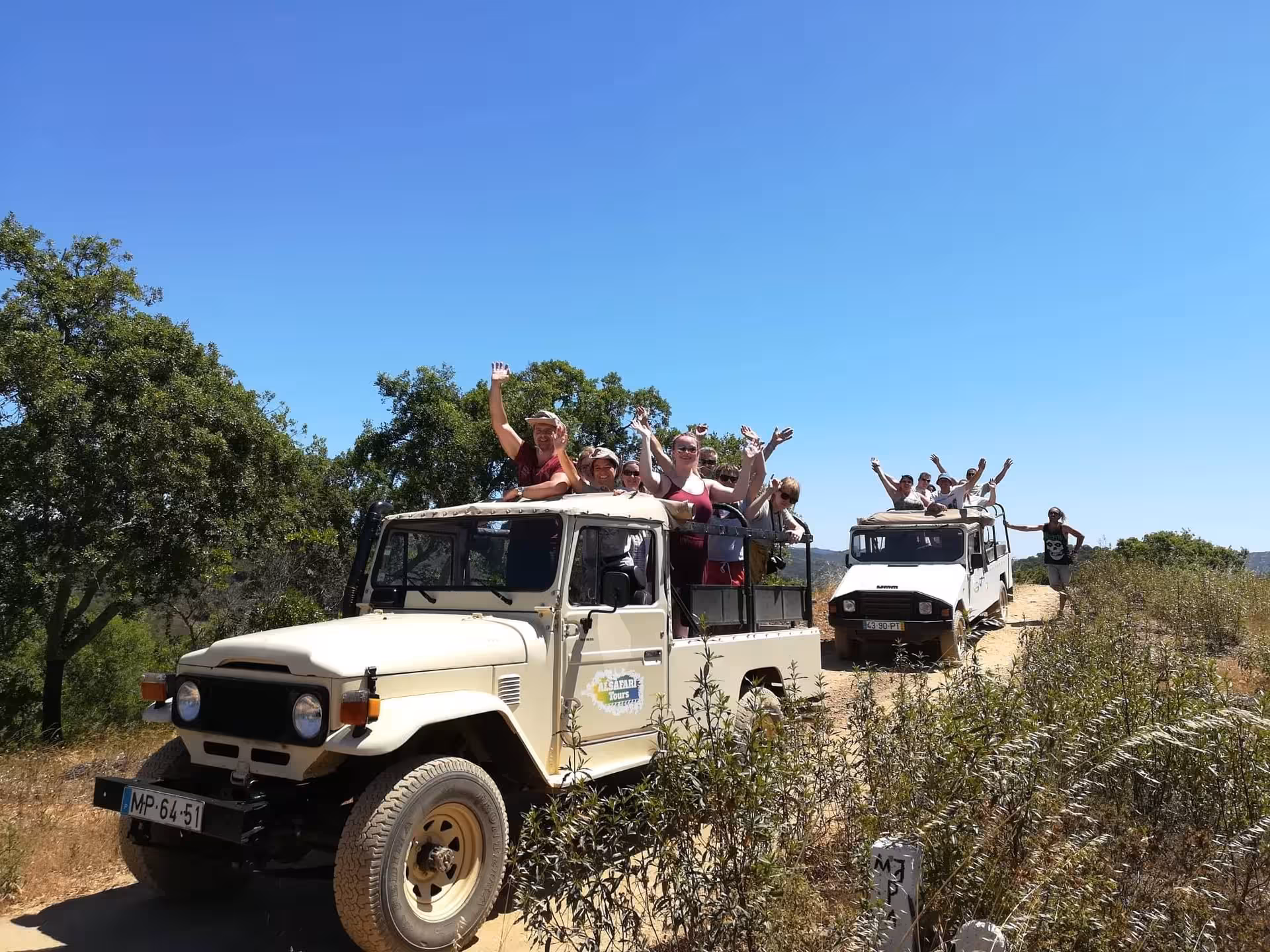 Open-top jeeps filled with excited travelers driving dusty Algarve trail under blue sky on guided off-road safari adventure