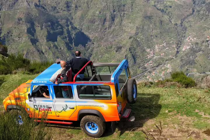 Vibrant jeep perched on Cabo Girão cliff edge during Madeira safari tour, offering breathtaking views of lush valleys below.