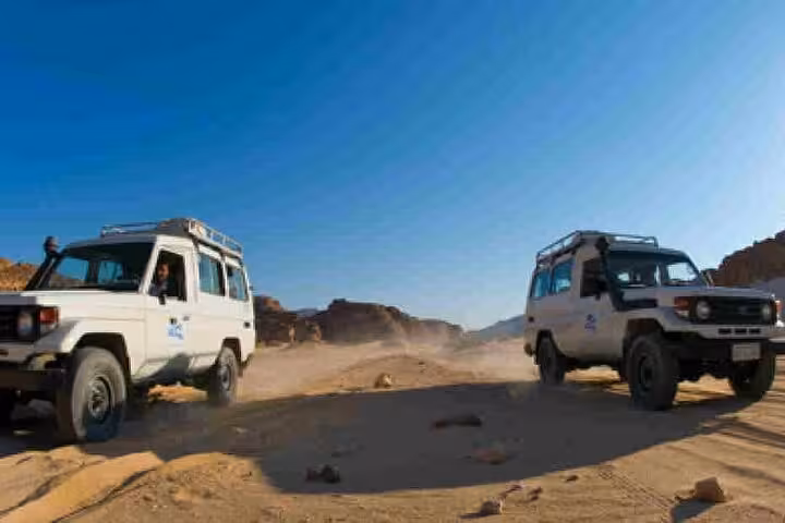 Two 4x4 jeeps racing across Marsa Alam desert on safari tour, kicking up dust on rocky sand track