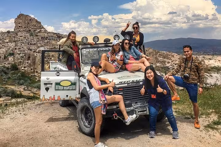 Group posing on 4x4 Jeep safari tour in Cappadocia with Uchisar Castle and fairy chimneys in the background