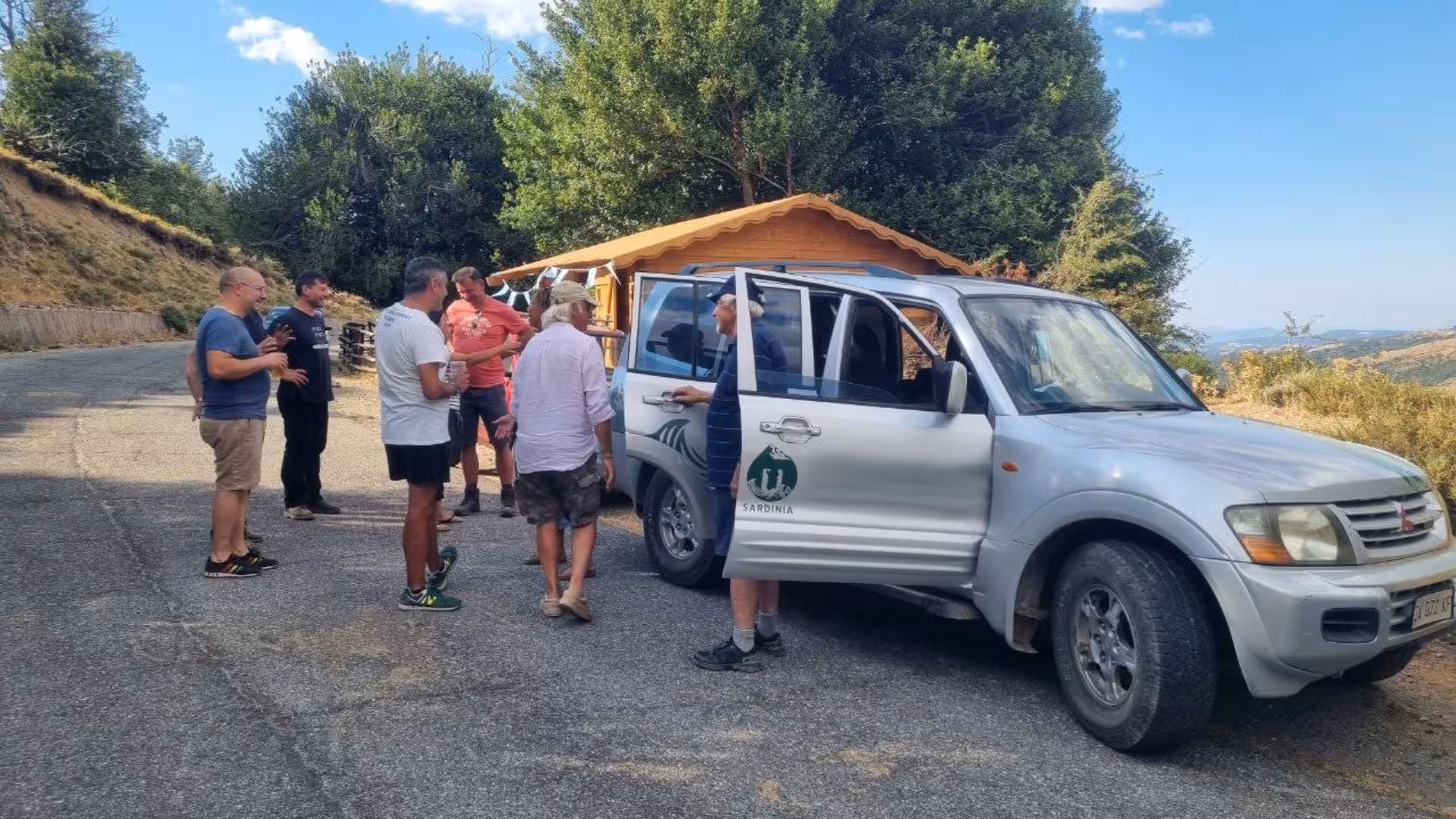 Group of tourists gather near a Jeep and wooden cabin during a Barbagia tour in Sardinia.