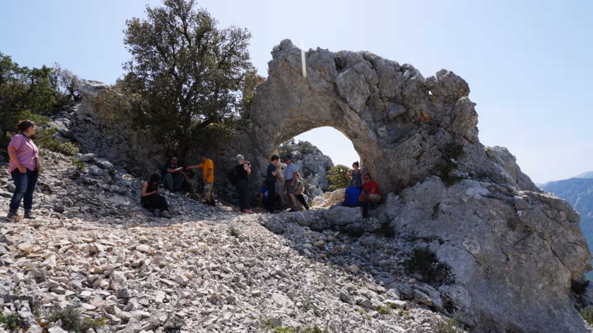 Visitors gathered at a scenic rocky arch in Supramonte, enjoying the breathtaking views on the Jeep tour from Cala Gonone.