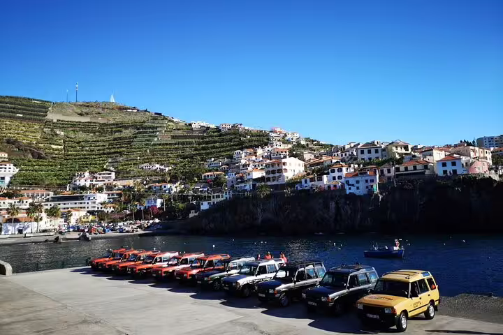 Jeeps parked by the waterfront in Câmara de Lobos with stunning terraced hills and coastal views in Madeira.
