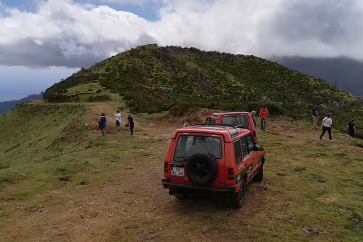 Tourists explore scenic hilltop with off-road Jeeps parked, offering panoramic views in Câmara de Lobos, Madeira.
