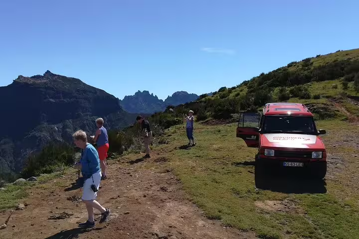 Tourists exploring scenic mountain landscapes with a red jeep during a half-day Câmara de Lobos adventure.