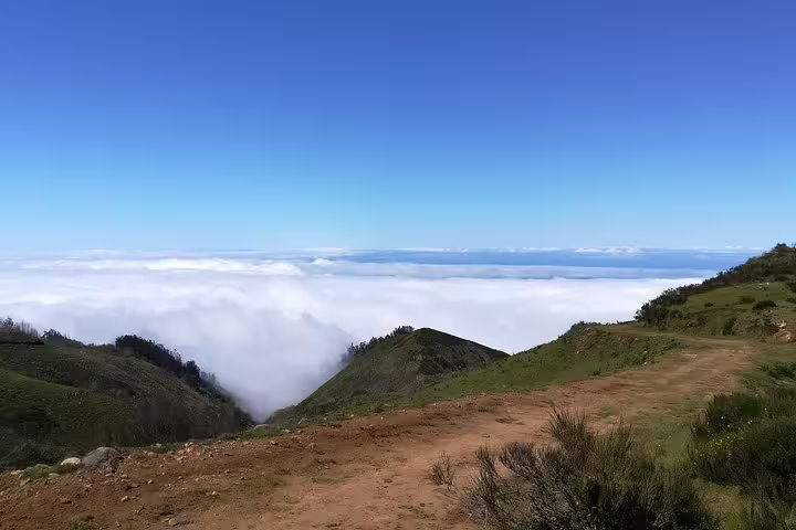 Scenic view from Câmara de Lobos jeep tour showcasing lush hills and clouds beneath a clear blue sky in Madeira.
