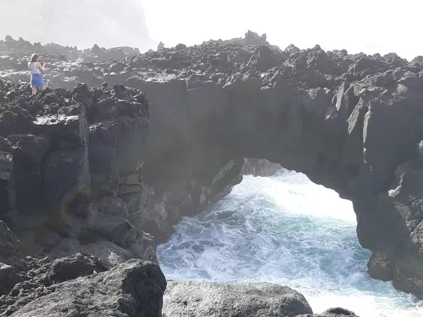 Traveler exploring rugged lava cliffs and natural ocean arch near Ferraria on a full-day Jeep tour from Ponta Delgada
