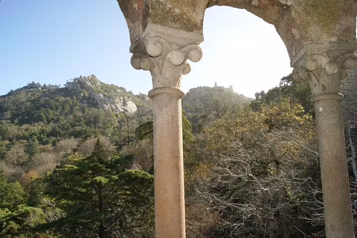 Majestic stone archway with a view of lush forested hills on the Sintra-Cascais Jeep Tour.