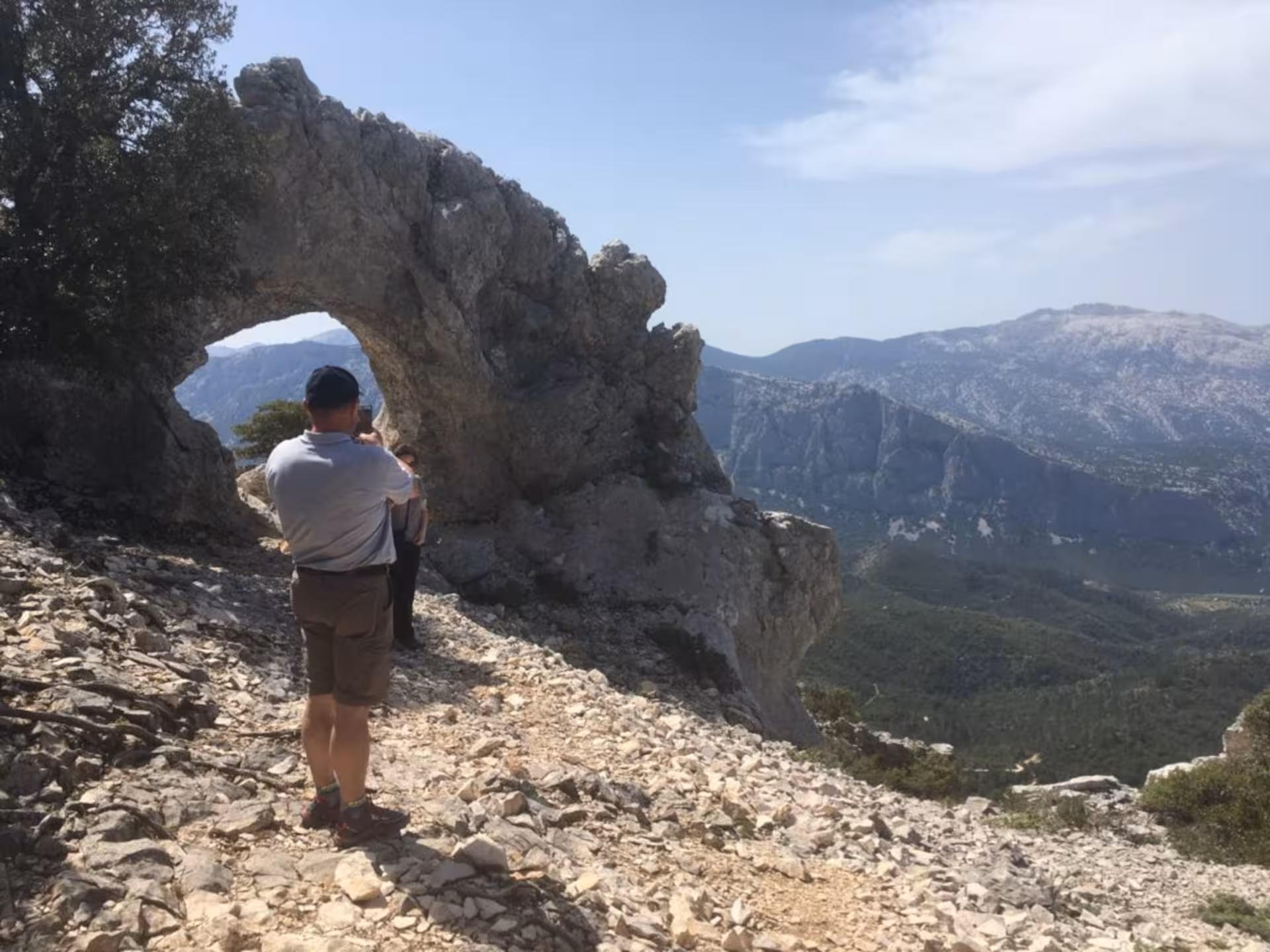 Tourist capturing the stunning rocky arch in Supramonte on a Jeep tour from Cala Gonone, Sardinia.