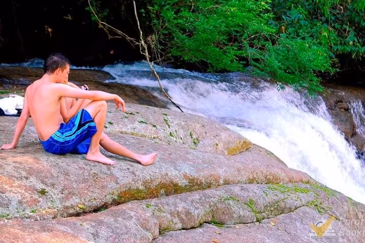 Relaxing by a serene waterfall, a young traveler enjoys the natural beauty on a Jeep tour adventure.