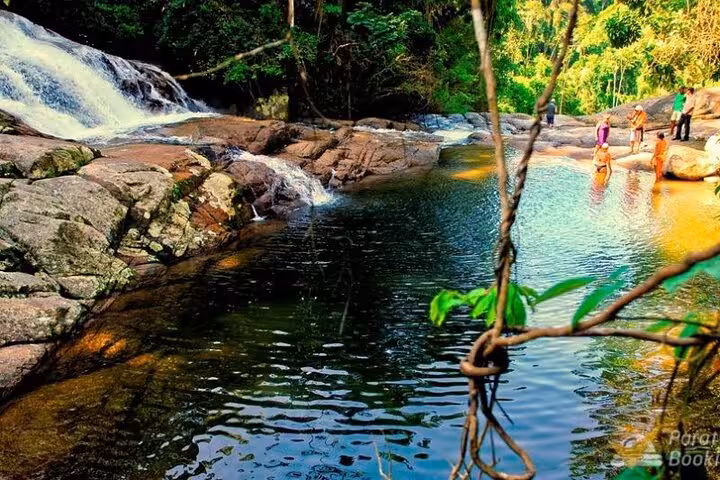Visitors enjoy a refreshing dip by a cascading waterfall during an adventurous jeep tour in lush greenery.