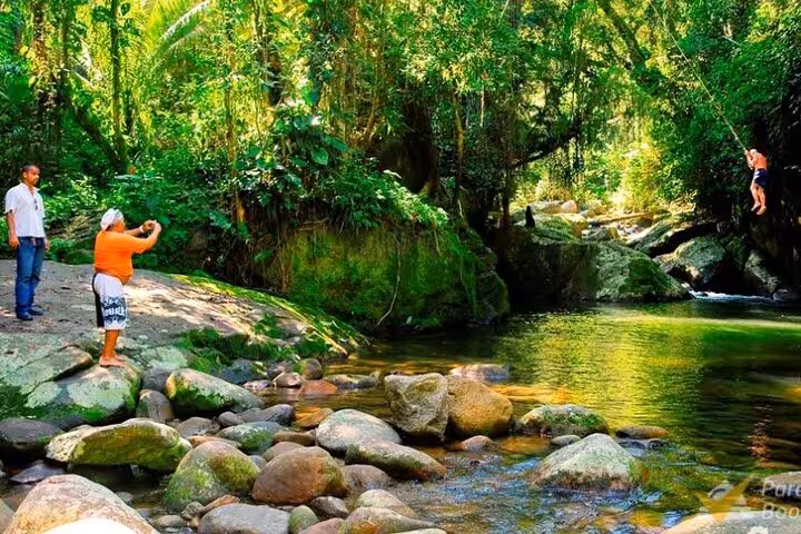 Tourists capture vibrant moments and swing by a serene stream on a scenic jeep waterfall journey.