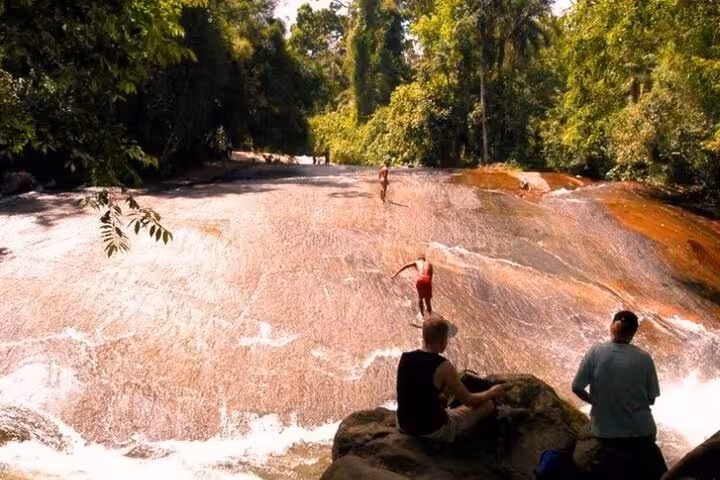 Adventurers slide down a natural rock slide as part of an exhilarating jeep tour through the forest.