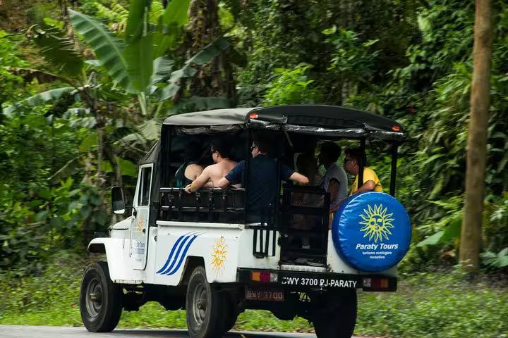 Open-air Jeep filled with tourists exploring lush rainforest on an exhilarating Jeep Tour to waterfalls.