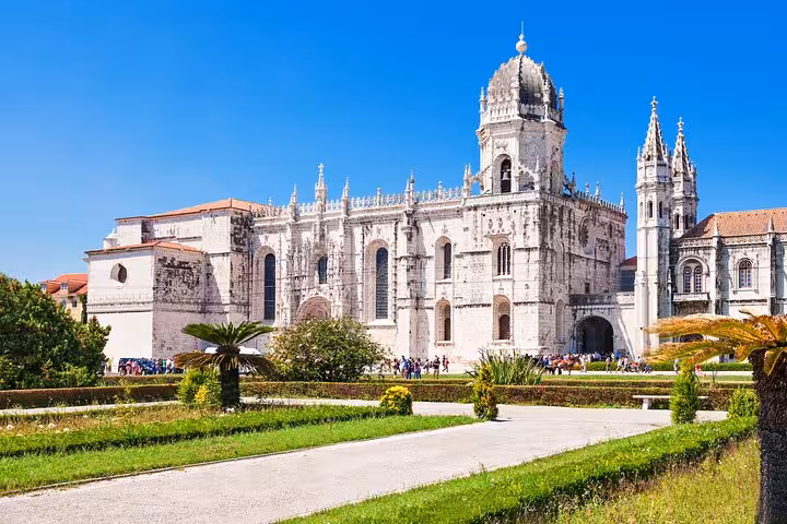 Front view of the magnificent Jerónimos Monastery in Belém, surrounded by lush gardens and vibrant greenery.