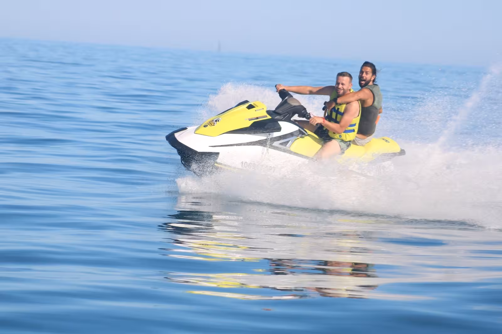 Two friends speeding on a yellow jet ski at Praia dos Tomates, enjoying an adrenaline-filled Algarve water sports tour.