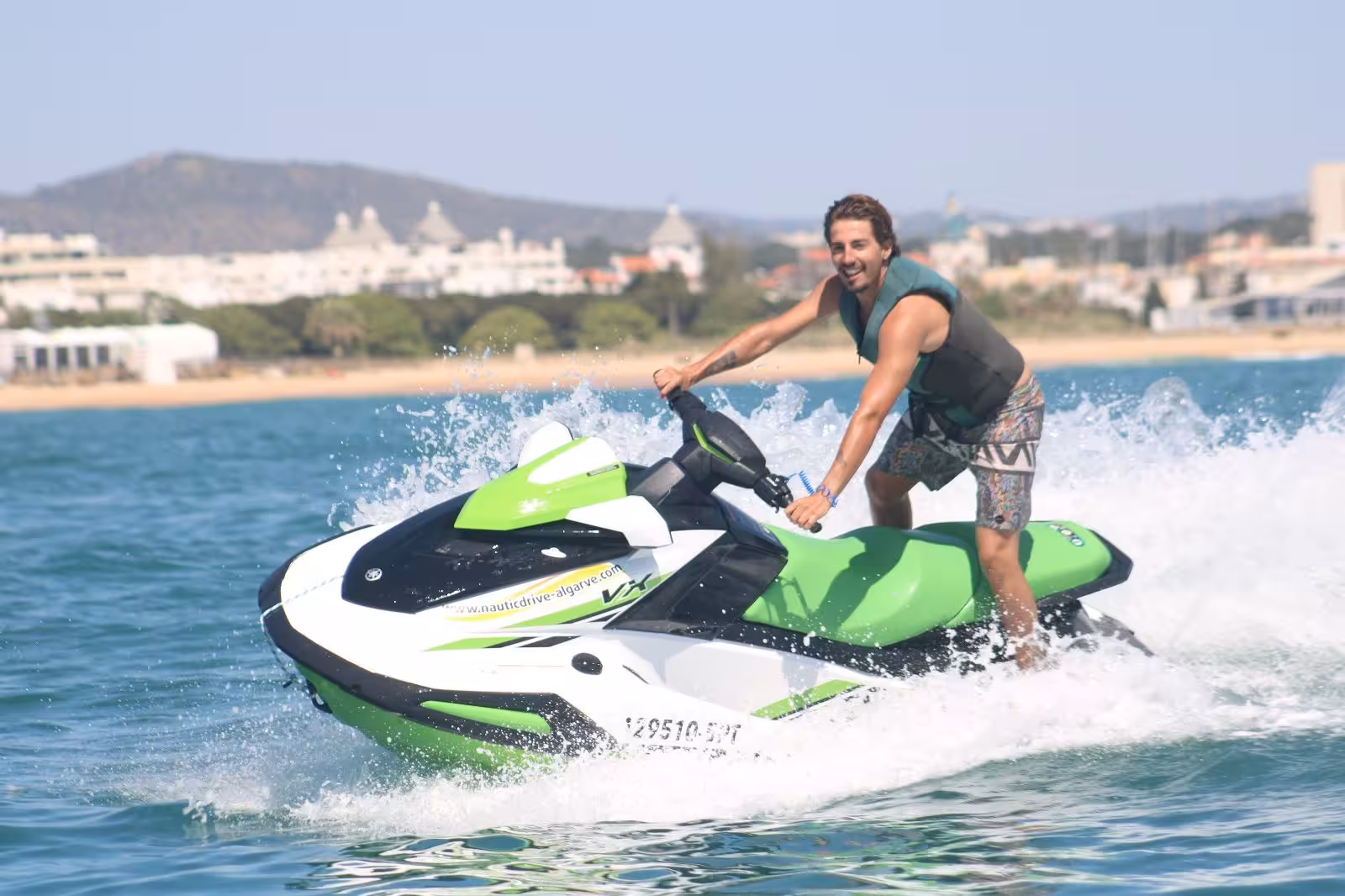 Young man standing on a green jet ski at Praia da Rocha Baixinha, enjoying Algarve jet ski rental on calm blue sea