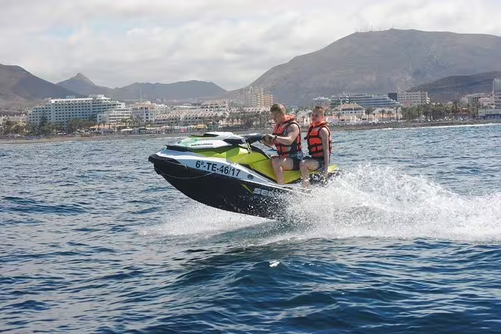 Thrilling jet ski safari with two riders gliding over waves near scenic coastal cityscape.
