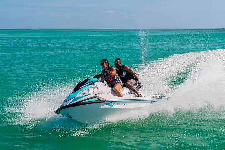 Two riders on jet ski from San Antonio Ibiza to Atlantis, fast turn on crystal sea during guided tour