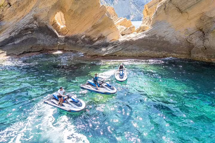 Jet ski tour from San Antonio Ibiza to Atlantis, riders in turquoise cove beneath dramatic sea cliffs