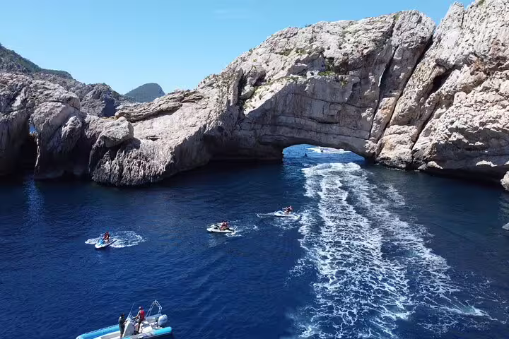 Jet skis cruising from San Antonio Ibiza to Margaritas Islands, passing a sea cave arch on blue water