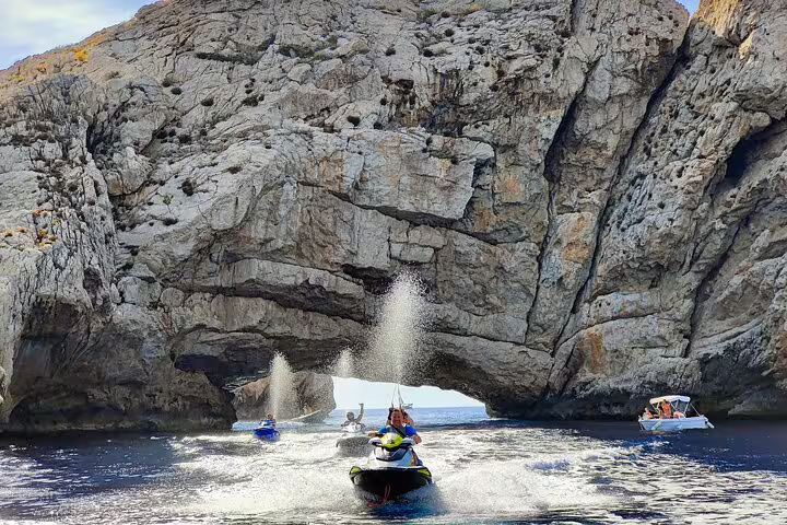 Riders speeding on jet skis to Margaritas Islands from San Antonio Ibiza by dramatic rock arch