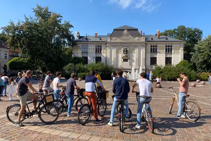 Cyclists gather in front of a historic building in the Jewish Quarter, enjoying a sunny day on a guided bike tour.