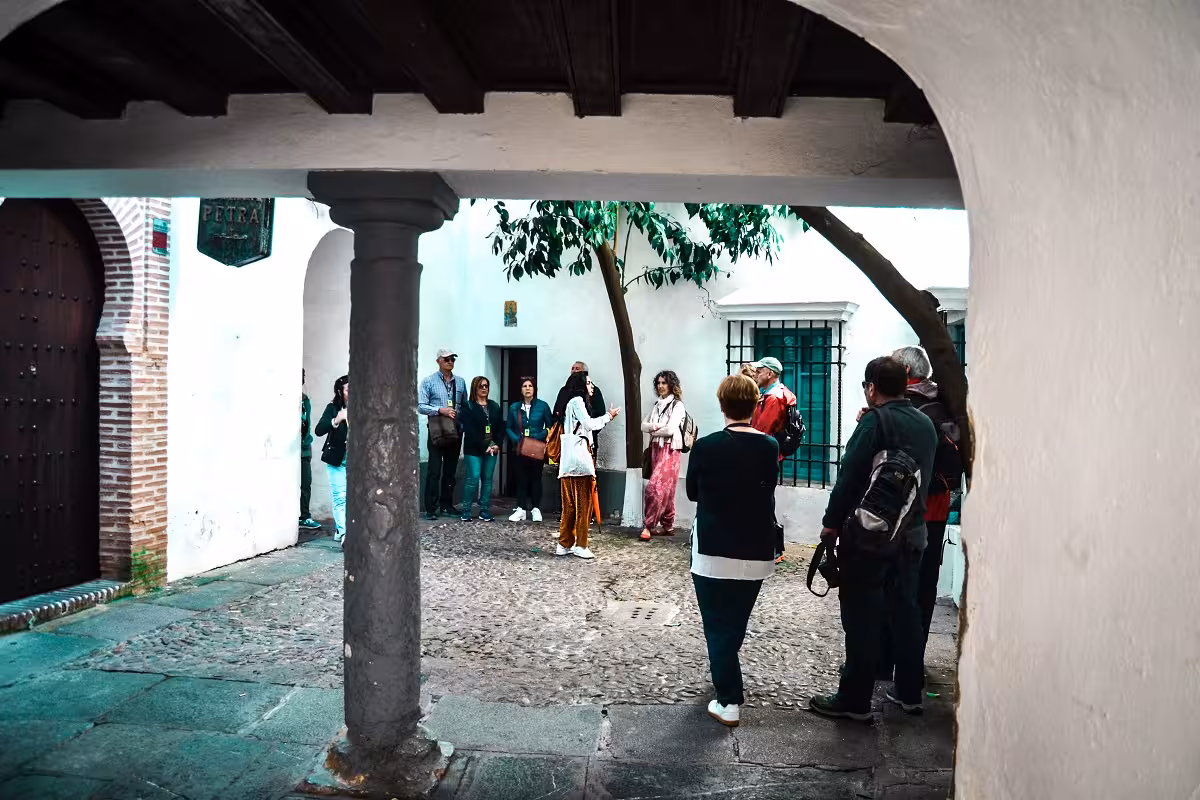Tour group exploring the historic Jewish Quarter in a cobblestone courtyard with whitewashed walls.