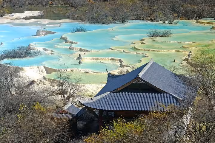 Traditional Chinese architecture nestled by the vibrant blue terraced pools of Jiuzhaigou.