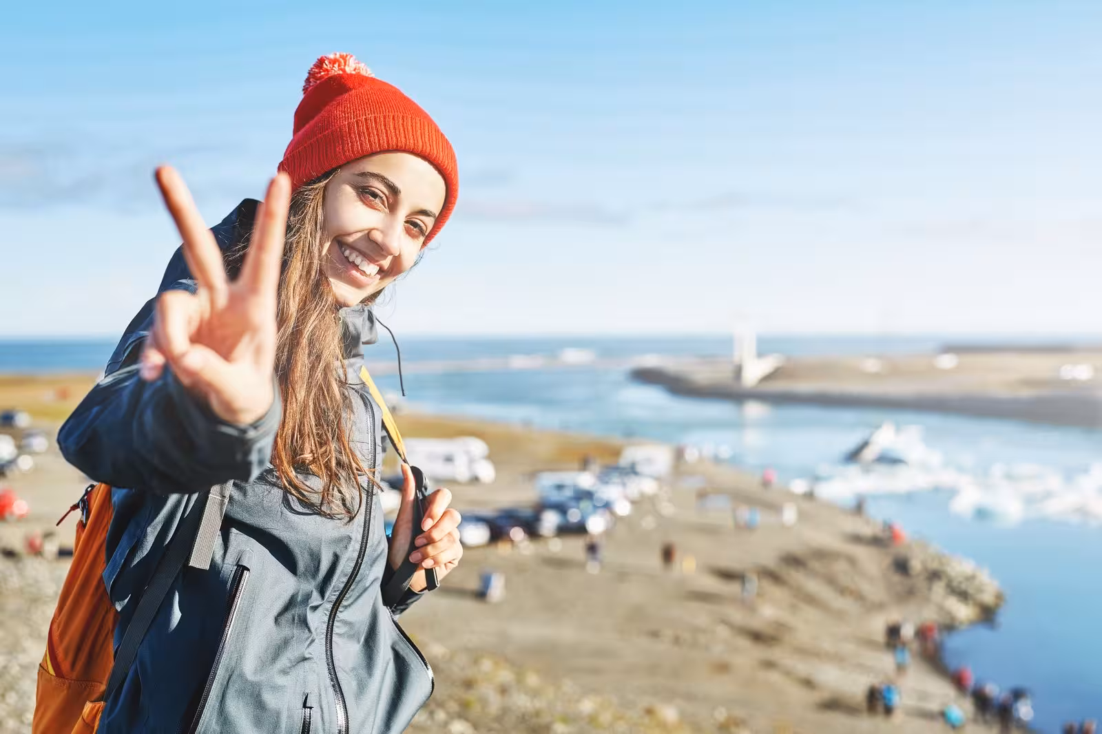 Smiling tourist flashes peace sign at Jokulsarlon Glacier Lagoon on a sunny day during the 3-Day Northern Lights Tour.
