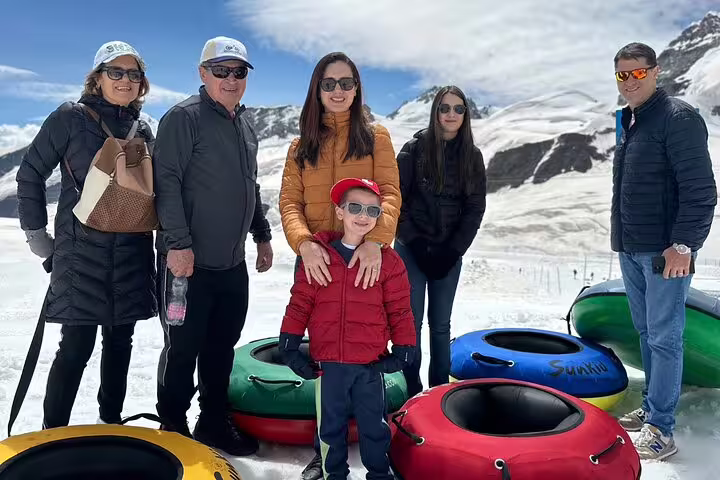Family enjoying snow tubing adventure on Jungfraujoch day trip with stunning Alpine views in the background.