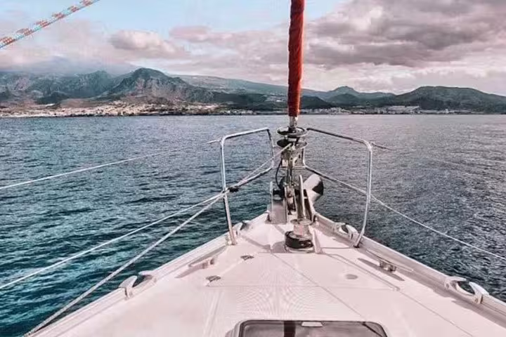 Front view from Kailani Sailing Yacht cruising towards scenic coastal mountains under dramatic skies.
