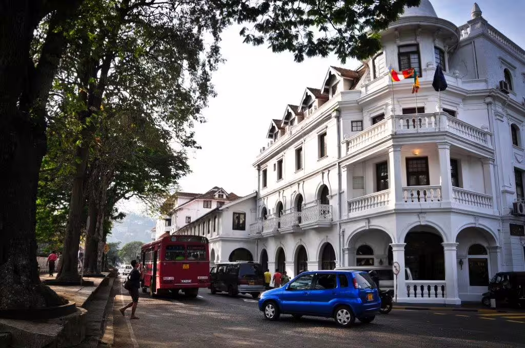 Historic colonial architecture and bustling street scene in Kandy, Sri Lanka, featuring local vehicles and greenery.