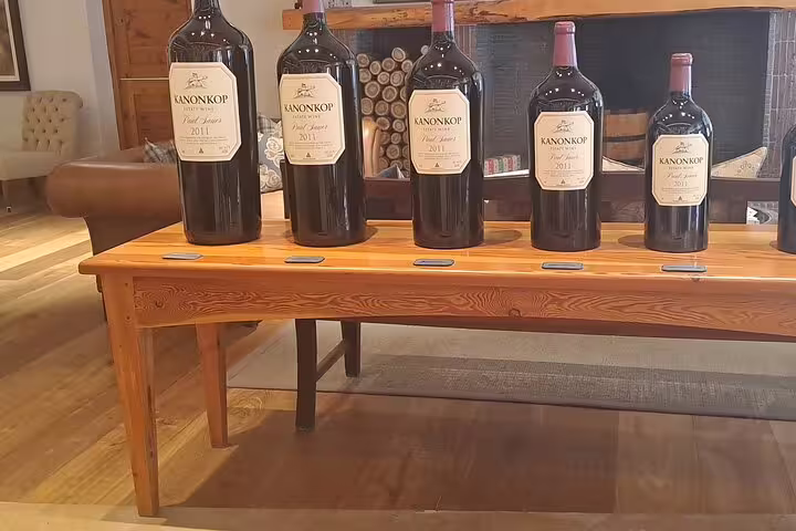 Large Kanonkop wine bottles displayed on a wooden table in a cozy Franschhoek wine tasting room.