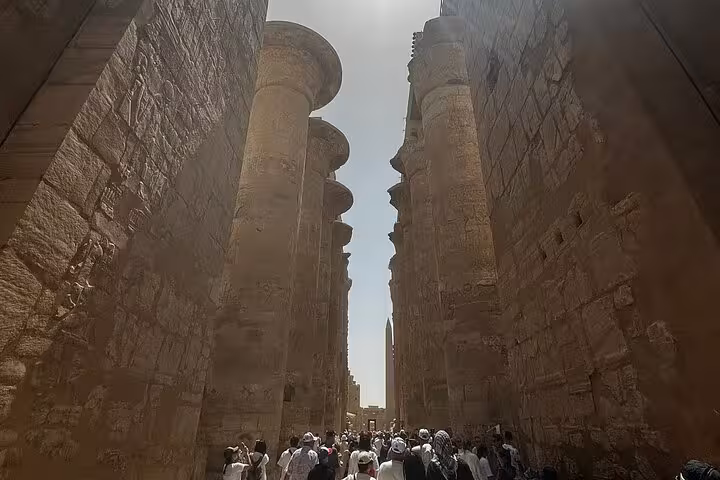 Visitors explore the towering columns of Karnak Temple under the bright sun, showcasing its majestic ancient architecture.
