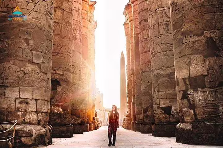 Sunlit corridor between carved columns at Karnak Temple, Luxor East Bank tour with ancient obelisk view