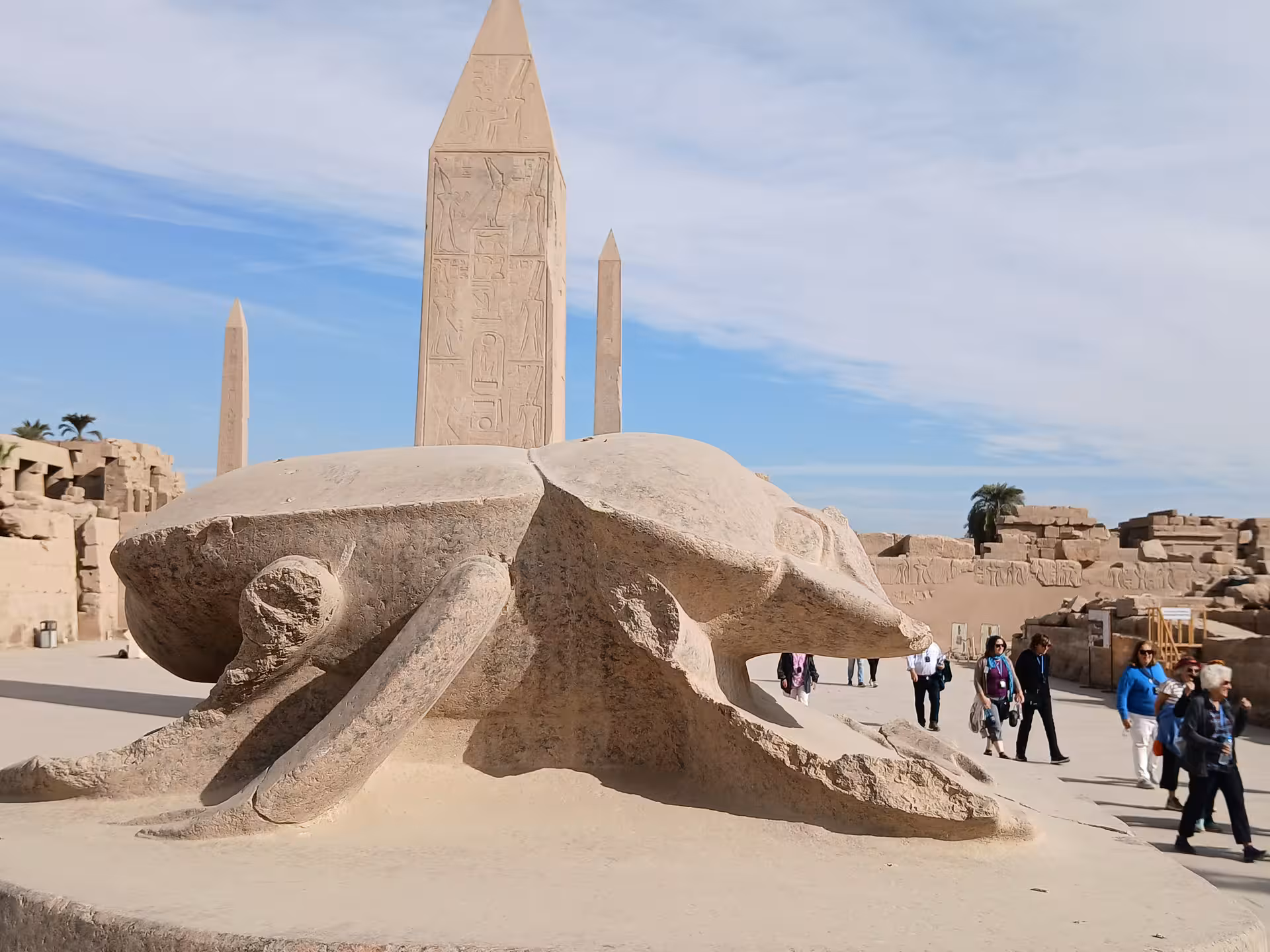 Tourists exploring the ancient Karnak Temple complex in Luxor, featuring a prominent scarab statue and obelisks.