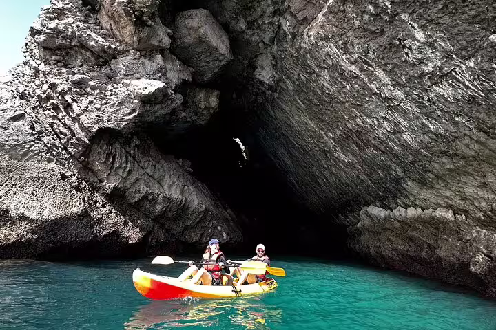 Adventurers kayaking through crystal-clear waters and exploring stunning caves in Sesimbra's Arrábida Natural Park.