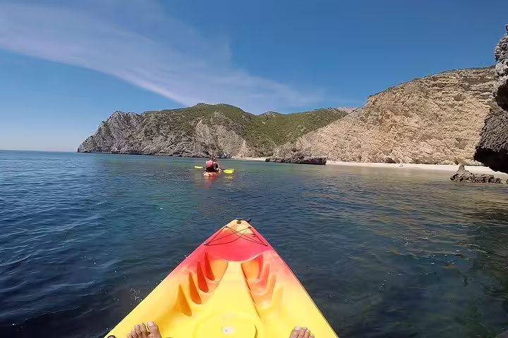 Kayak adventure in Sesimbra showcasing vibrant kayaks navigating crystal-clear waters and stunning cliffs in Arrábida Natural Park.