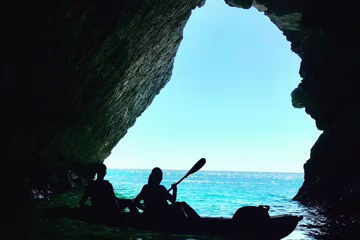 Kayakers explore a stunning sea cave in Sesimbra, Arrábida Natural Park, with crystal-clear waters and a sunlit ocean view.