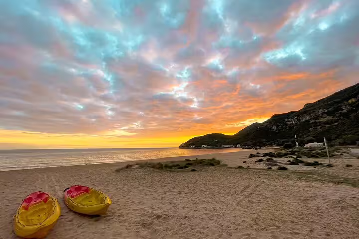 Two kayaks rest on a sandy beach at sunset in Lisbon, ideal for a full day kayak and coasteering adventure tour.