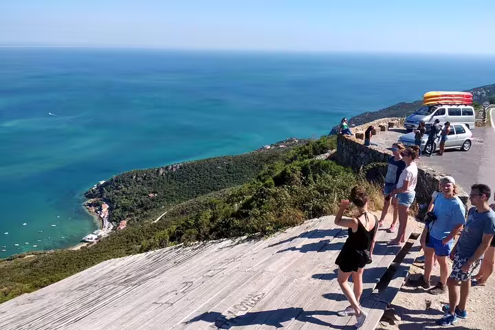 Tourists enjoying a scenic ocean view on a cliffside stop during a full-day kayak and coasteering adventure from Lisbon.