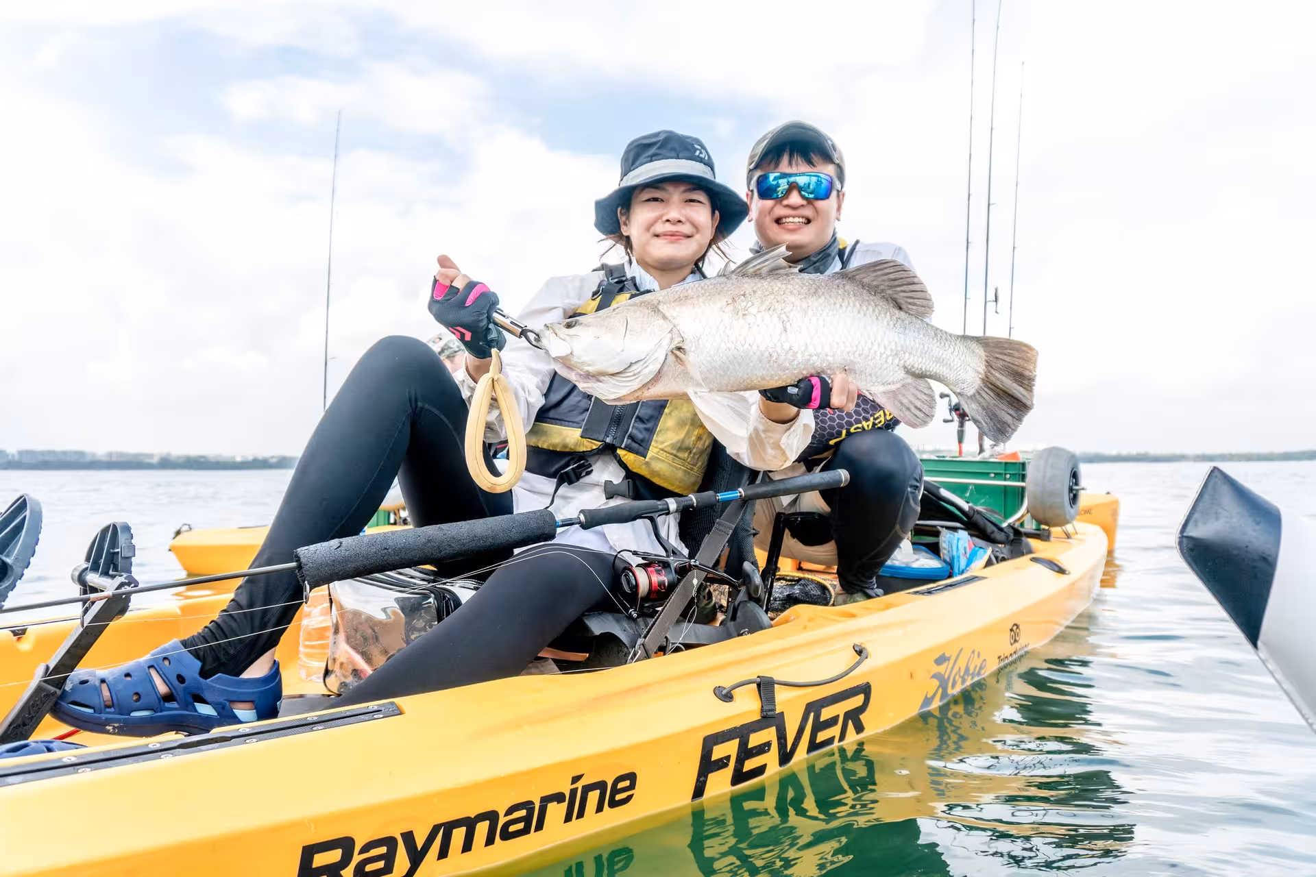 Two kayakers proudly show off their catch on a yellow kayak during a Pulau Ubin fishing trip.