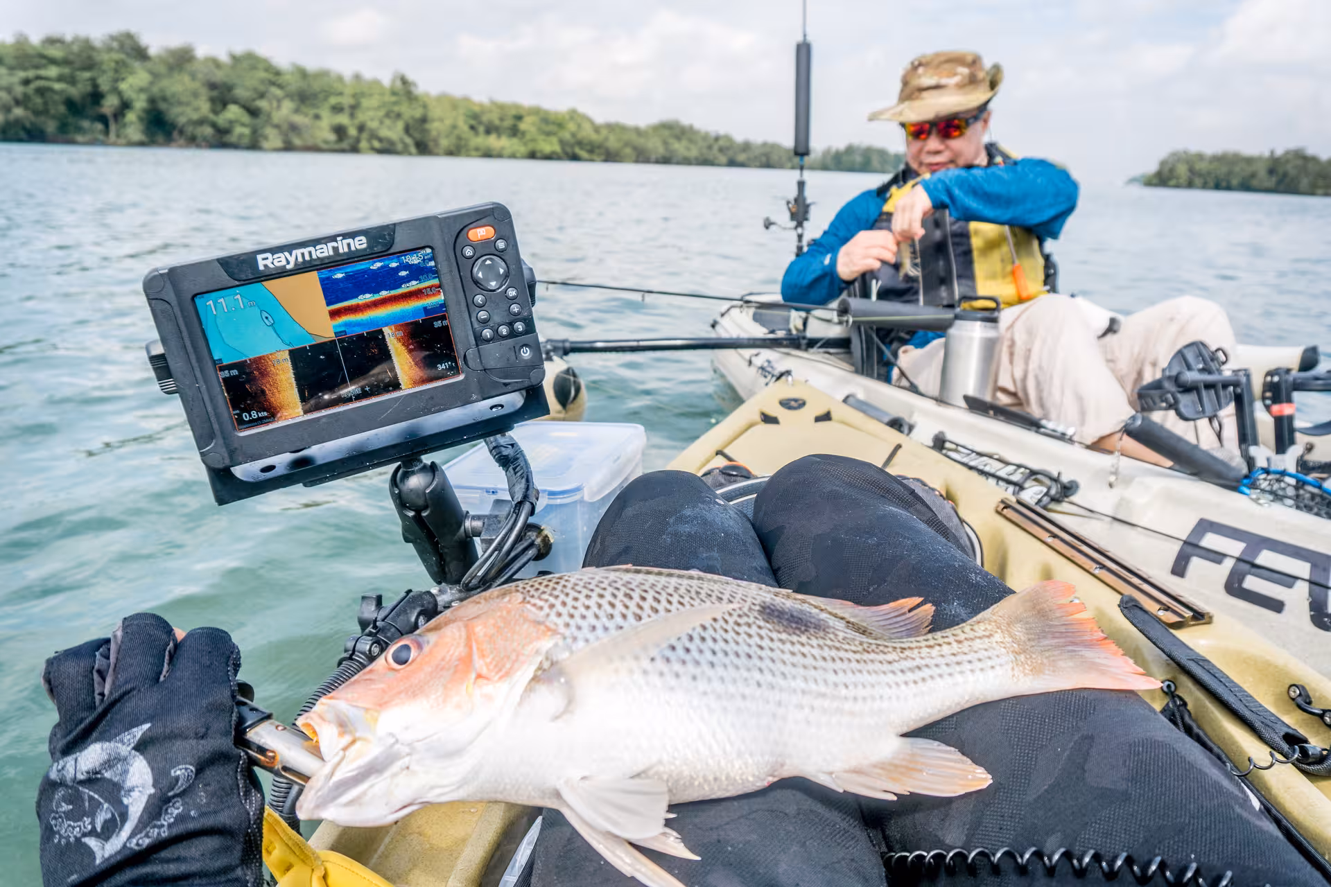 Kayak fisher displays catch with fish finder nearby, enjoying Pulau Ubin's scenic waters.